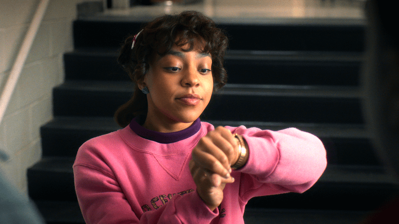 Priah Ferguson as Erica looking at her watch while wearing a pink sweater in Stranger Things 5