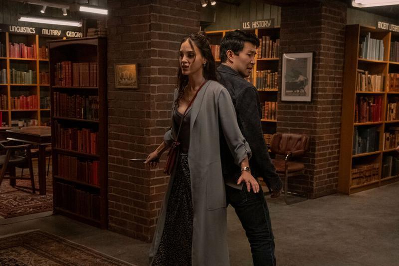 Melissa Barrera as Michelle and Simu Liu as Alexander Hale fighting back-to-back in a library in The Copenhagen Test.