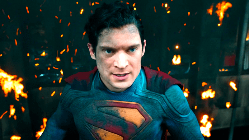 David Corenswet as Superman flying in front of a flaming building in Superman