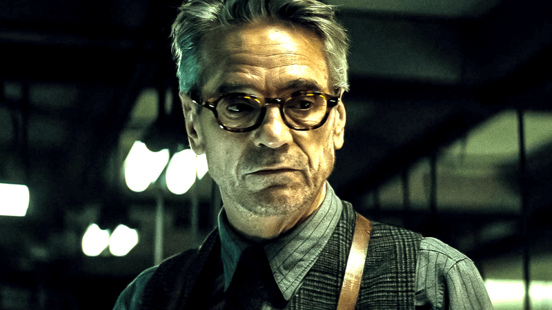 Jeremy Irons as Alfred in a pair of glasses standing in the Bat Cave in Batman v Superman