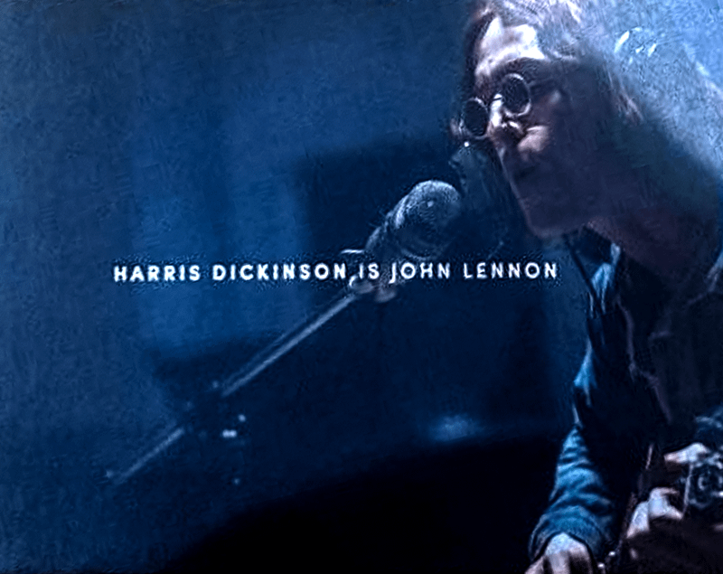 Harris Dickinson as John Lennon singing into a microphone and holding a guitar in a studio in The Beatles movie.