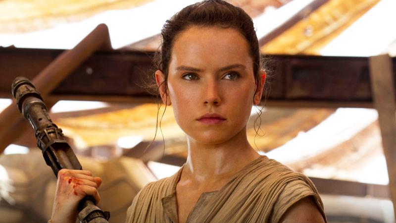 Daisy Ridley as Rey holding a metal staff in Star Wars: The Force Awakens.
