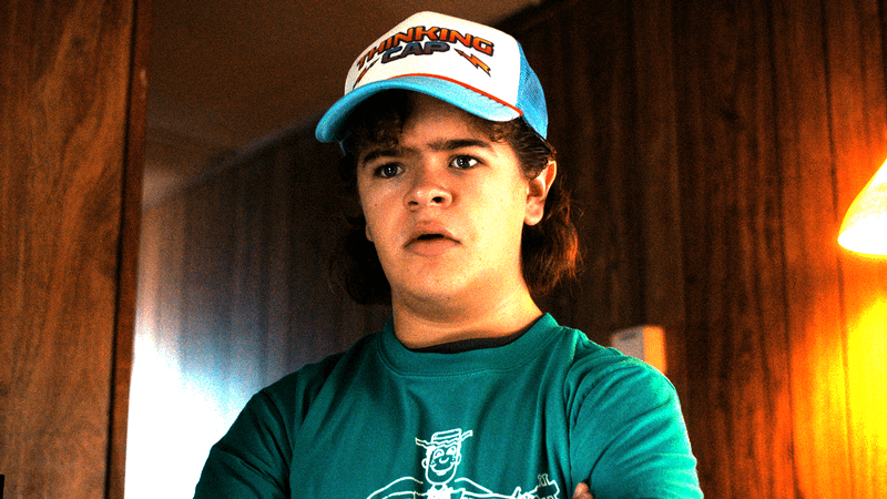 Gaten Matarazzo as Dustin in a trucker hat standing in a doorway in Stranger Things