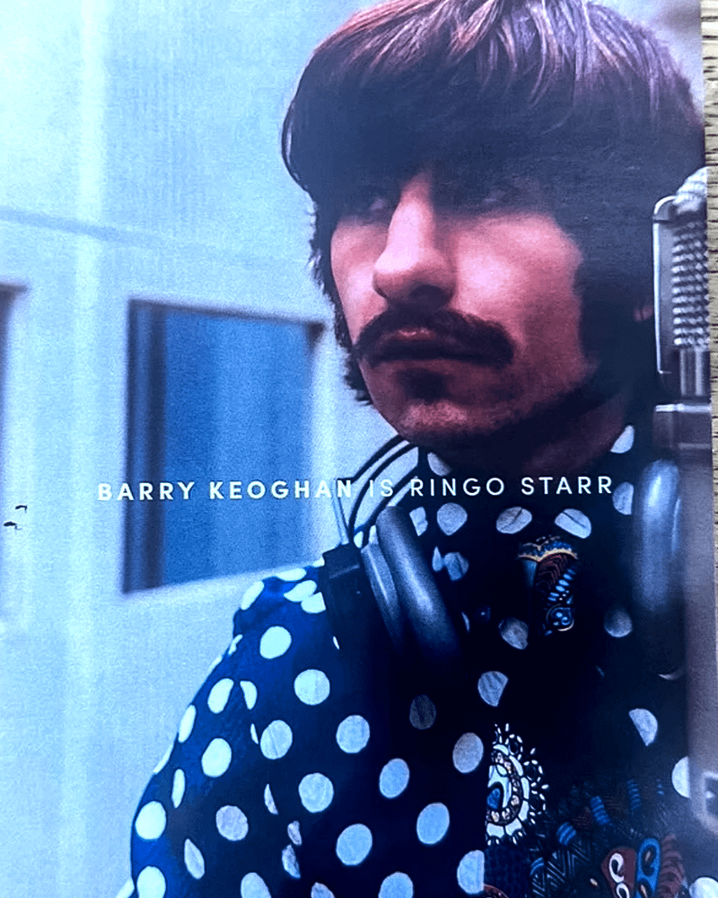 Barry Koeghan as Ringo Starr sitting at his drum set with some headphones on his neck in The Beatles movie.