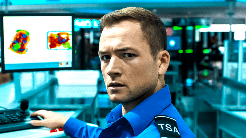 Taron Egerton as a TSA Agent standing next to a computer in Carry On
