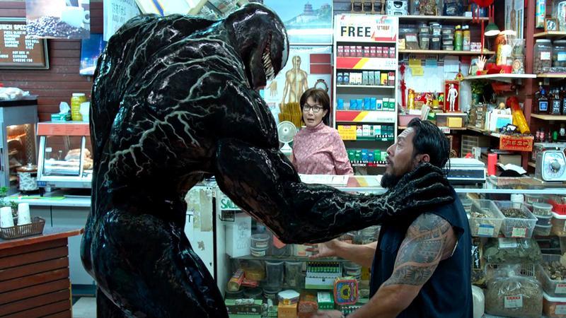 Tom Hardy as Eddie Brock holding the neck of a man in Venom