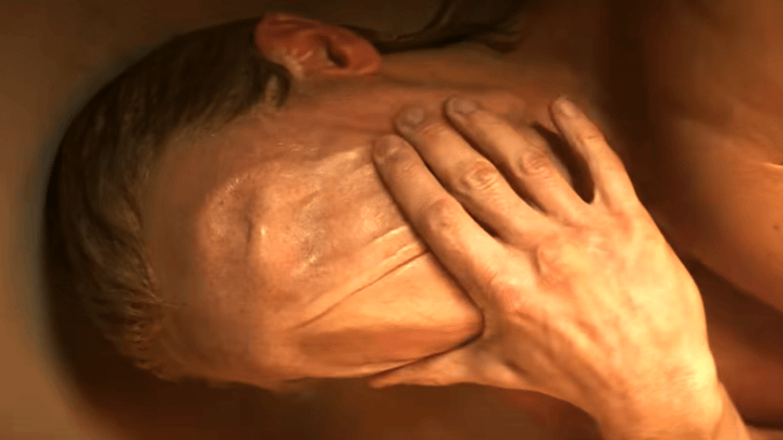 Matt Hagen wiping his hand over his face, leaving his eyes, nose, and mouth covered in clay-like skin.