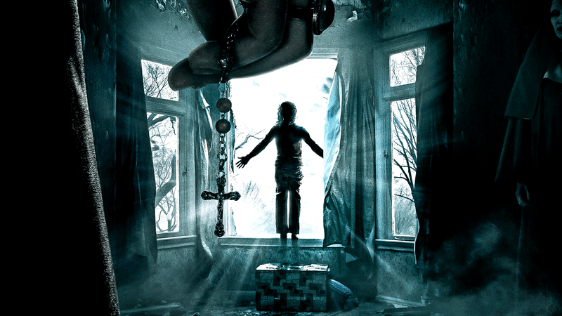 image from 'The Conjuring' of cross hanging from a hand behind woman standing at a window