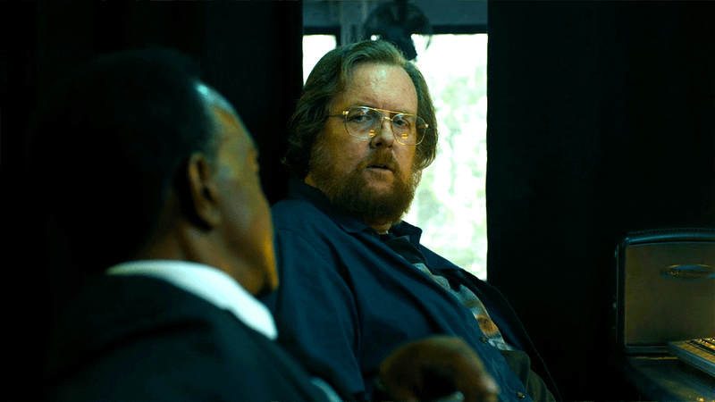 Steve Agee as Economos looking over at Tim Meadows as Fleury in Peacemaker