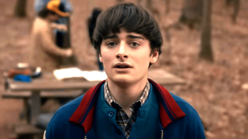 Noah Schnapp in a letterman jacket in the woods in Stranger Things 5