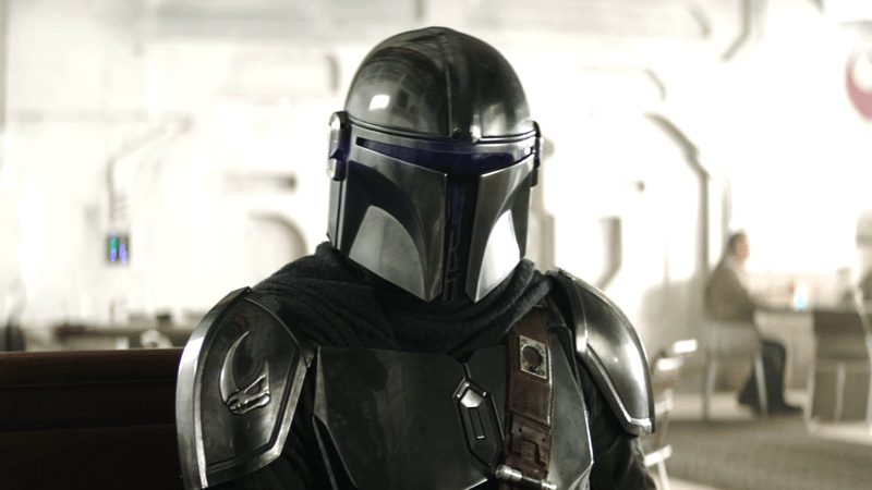 Pedro Pascal as Din Djarin sitting at a bar table in The Mandalorian & Grogu