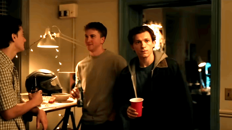 Peter Parker holding a red cup looking across the room.