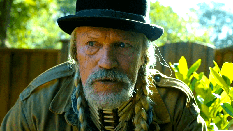 Michael Rooker as Red St. Wild leaning down on the ground in Peacemaker