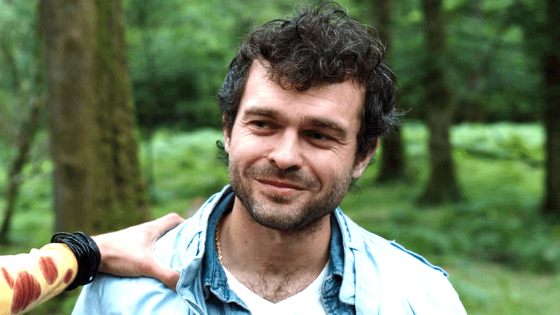 Alden Ehrenreich with a bit of stubble and a hand grabbing his shoulder
