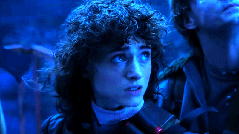 Natalia Dyer as Nancy Wheeler with curly hair standing in the dark in Stranger Things