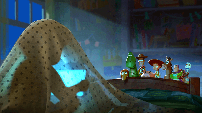 A child under a blanket with several toys looking over the edge of the bed at them in Toy Story 5