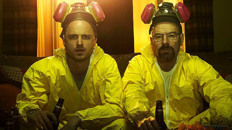 Aaron Paul as Jesse sitting next to Bryan Cranston as Walter White in some hazmat suits sitting on a couch in Breaking Bad