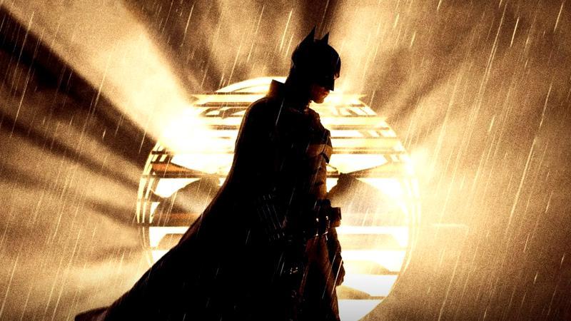 Robert Pattinson as Batman standing in the light of the bat signal in The Batman