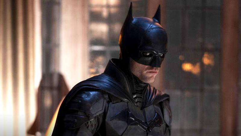 Robert Pattinson as Batman in his suit standing in a dimly lit room in The Batman