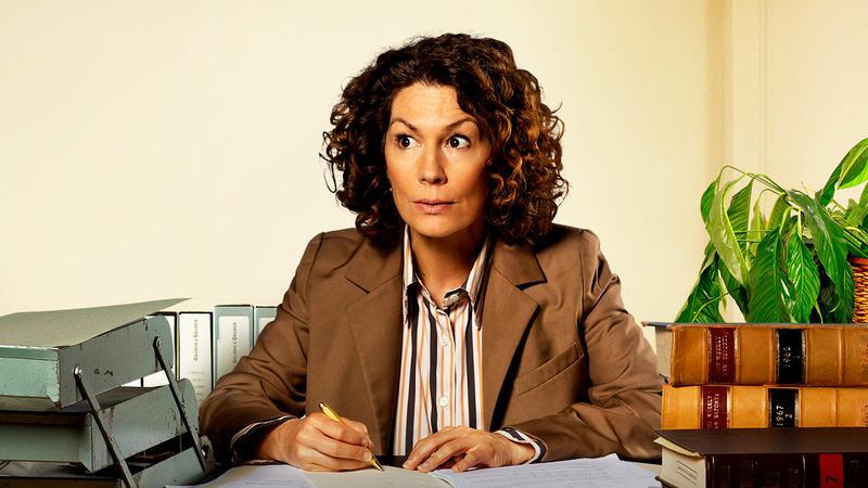 Kitty Flanagan as Fisk sitting behind a desk in Fisk
