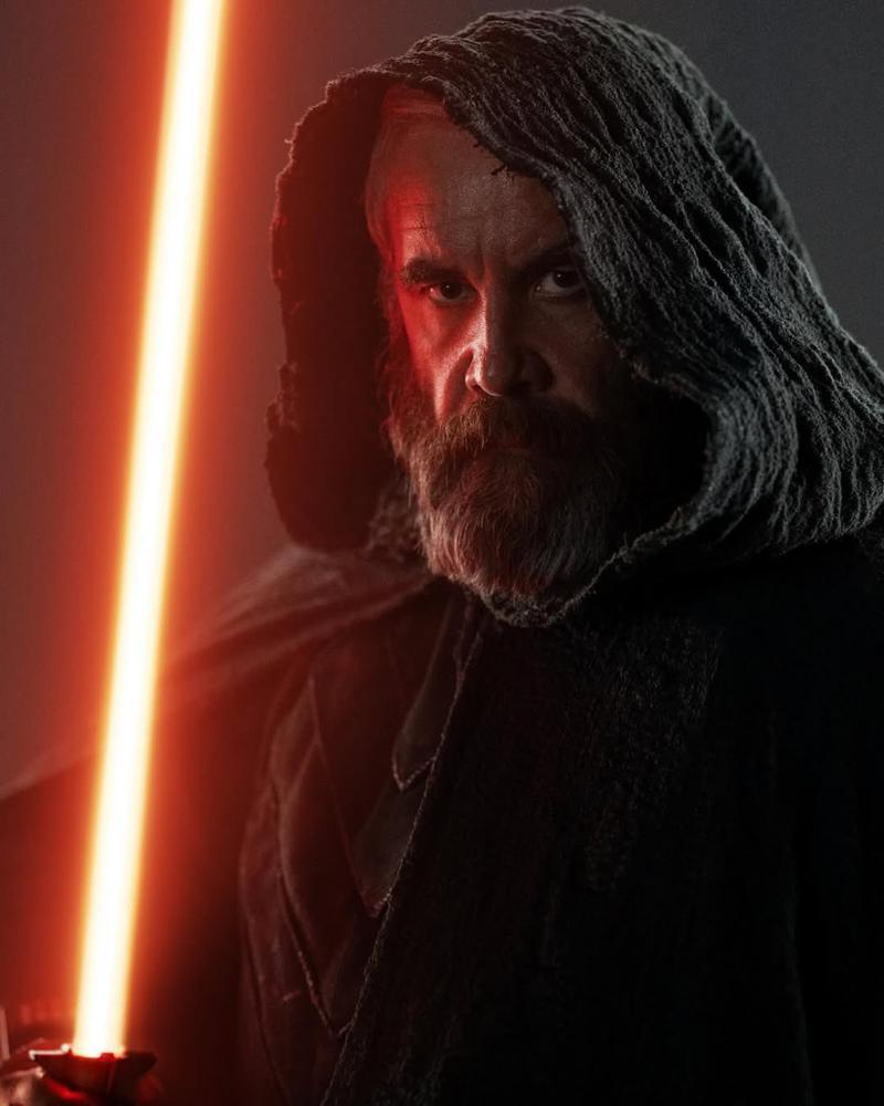 Rory McCann as Baylan Skoll holding an orange lightsaber to his face