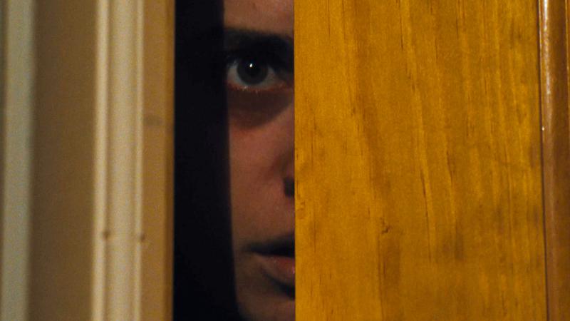 Theo looking out of a cracked door to avoid her captors in Godmother.