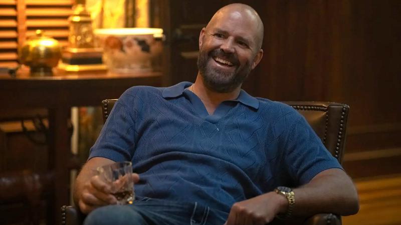David Denman as Captain Triumph sipping a drink leaning back in a chair in Peacemaker Season 2