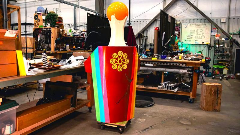 Meow Wolf Los Angeles work in progress art of a rainbow and red cylinder structure with an orange ball on top of it.