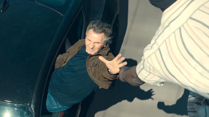 Liam Neeson reaching out of his car to grab on to a friend in Mongoose.