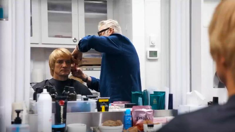 Nathan Fillion with a man cutting his hair in a styling chair in Superman
