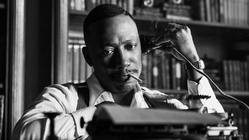 Lamorne Morris as Robbie Robertson at Typewriter in Spider-Noir in black and white.