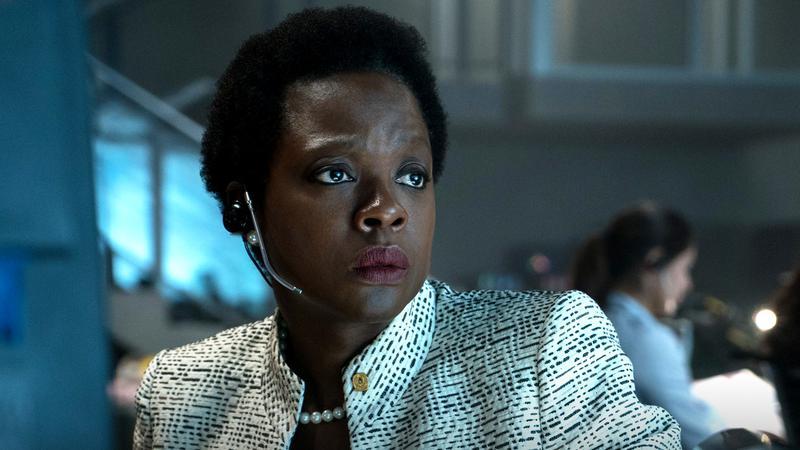 Viola Davis as Amanda Waller sitting in a desk with a headset on and a white speckled jacket in The Suicide Squad