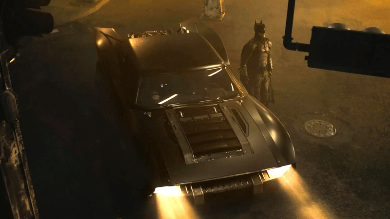 Robert Pattinson as Batman standing next to the Batmobile in The Batman