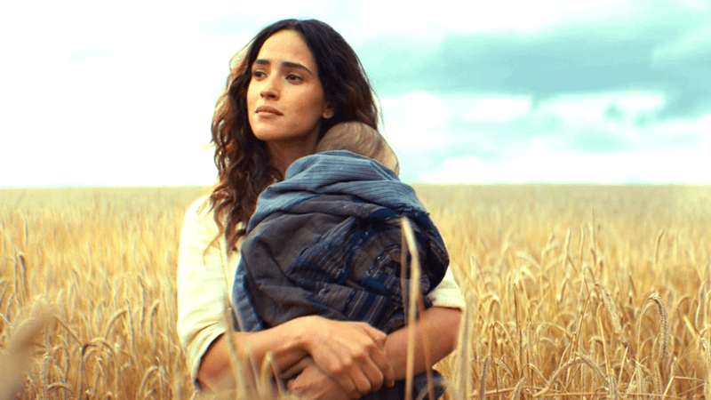 Adria Arjona as Bix Kaleen holding a baby in a field in Andor Seaosn 2 
