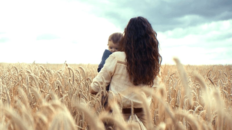 The back of Adria Arjona holding a baby in a field in Andor