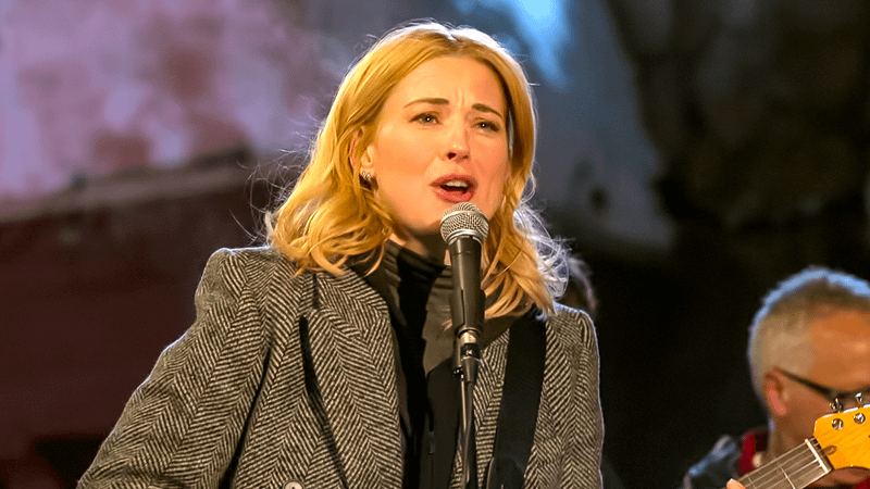 Alexandra Breckenridge as Taylor Jacobsen on a stage singing with a guitar in her hand in My Secret Santa