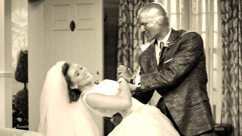 Elizabeth Olsen as Wanda Maximoff in a wedding dress being dipped by Paul Bettany as Vision in a suit jacket in WandaVision