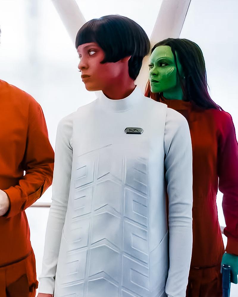 A close-up of the previous photo, focusing on Melchior. From left to right are some of Peter Quill, Daniela Melchior (unknown role), and Gamora. All but Melchior are wearing orange jumpsuits, while Melchior, who has an orange race, wears a white outfit. The background is white.