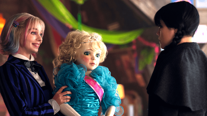 Emma Myers as Enid standing with a doll across from Jenna Ortega as Wednesday in Wednesday Season 2