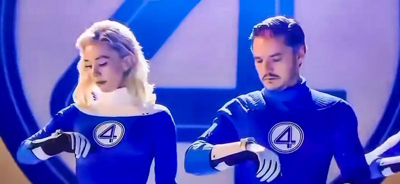 Vanessa Kirby as Sue Storm and Pedro Pascal as Reed Richards wearing their Fantastic Four costumes and looking at their wrists in The Fantastic Four: First Steps