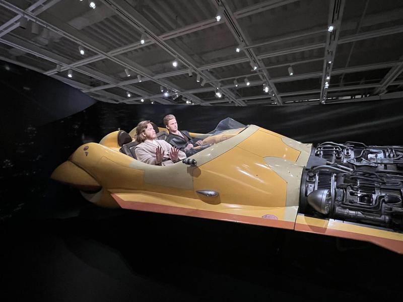 Life-size model of Obi-Wan Kenobi and Anakin Skywalker flying in yellow vehicle from 'Star Wars: Episode II — Attack of the Clones.'