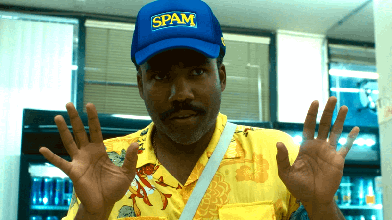 Donald Glover posing in a yellow shirt and SPAM hat in Bardo Stone & the New World movie