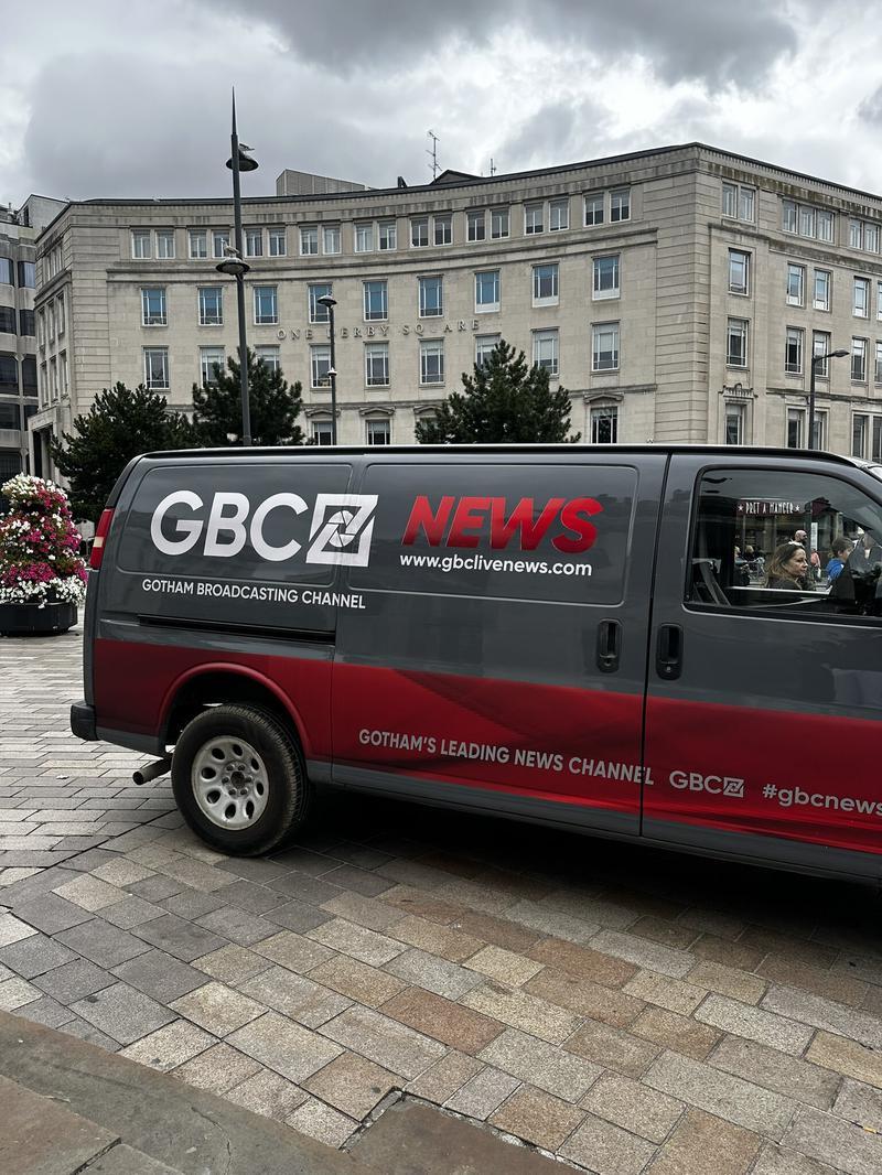 Gotham Broadcasting Channel news van in front of tan building on Clayface set