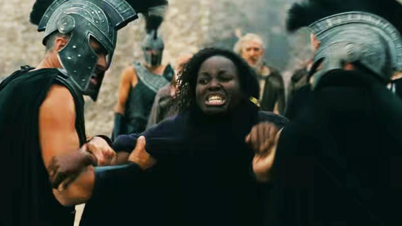 Lupita Nyong'o as Clytemnestra in The Odyssey, restrained by soldiers.