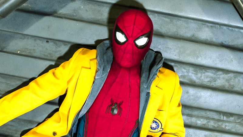Masked Spider-Man lying down with yellow Midtown School jacket on.