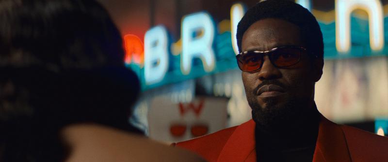 Yahya Abdul-Mateen II as Simon Williams wearing red-tinted sunglasses and a red suit jacket in