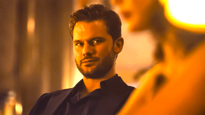 Jeremy Irvine as Zach in a black suit sitting in a warmly lit room in Turbulence