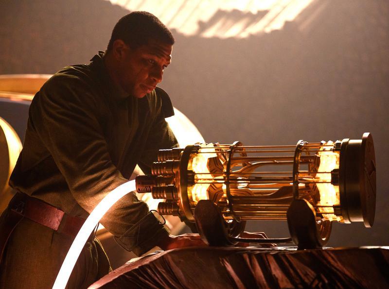 A screenshot of Kang, seeming to be in his time chair, working on a machine that appears to be a battery or energy core of some sort. It glows yellow, and the picture has a brown hue to it.