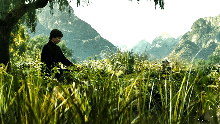 Luke Skywalker sitting in front of Grogu on the grass with mountains behind them.