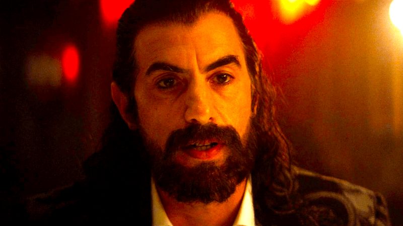 Sacha Baron Cohen as Mephisto sitting in a dark bar in Ironheart